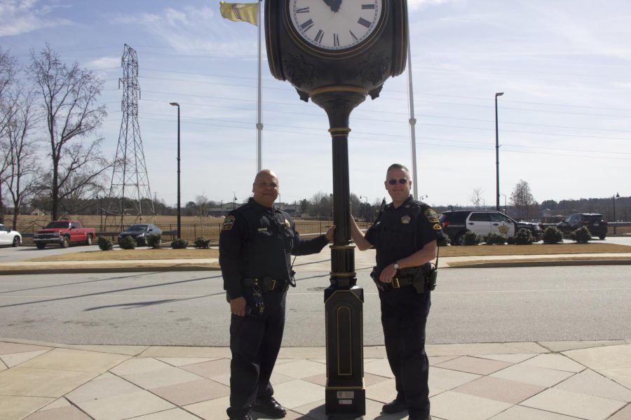 Standing together, the two officers stand in front of the school that they love the most.