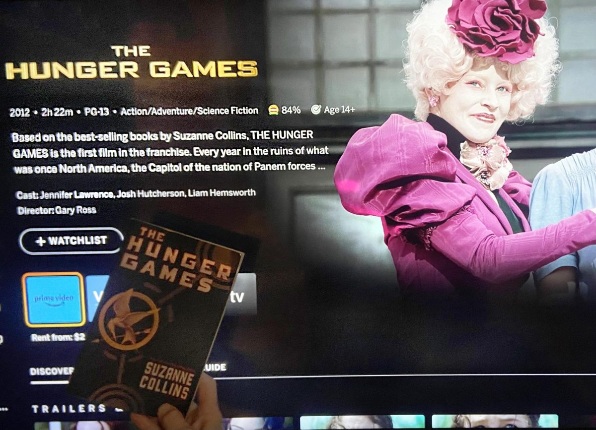 The original Hunger Games book in front of the Hunger Games movie on the big screen.