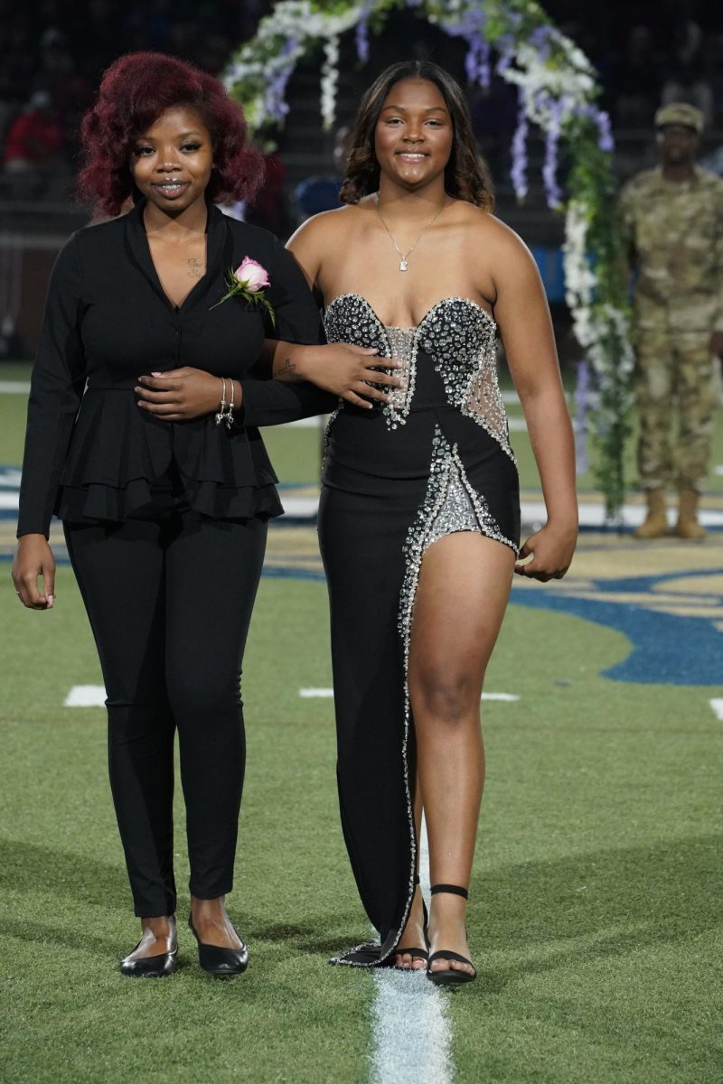 Kamryn Sainvil (12) and her escort smile as they walk down the field for Homecoming Court. 