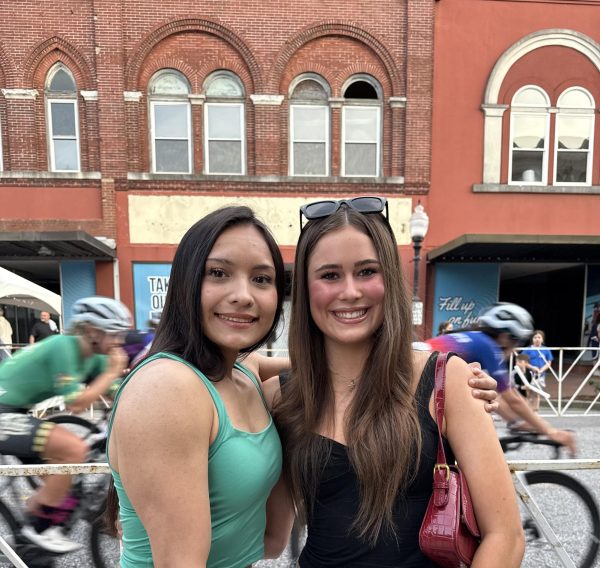 Chatavia Huff (12) and McKenna Brown (10) pose for a picture while pro-cyclists race behind them. 