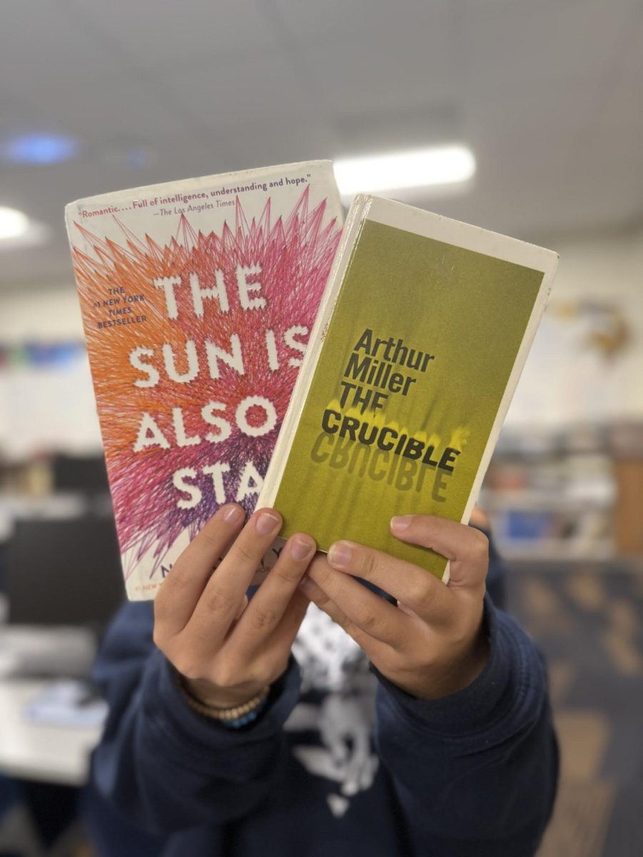 A student holds up two books: "The Sun is also a Star" for personal enjoyment and "The Crucible" for school.